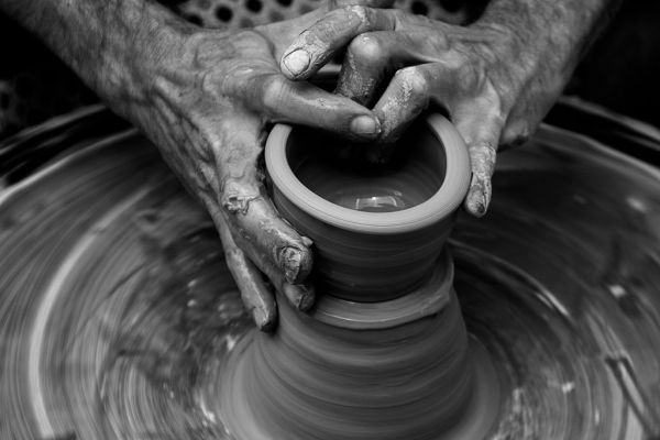 Black-and-white photograph of an artist shaping a vessel on a pottery wheel